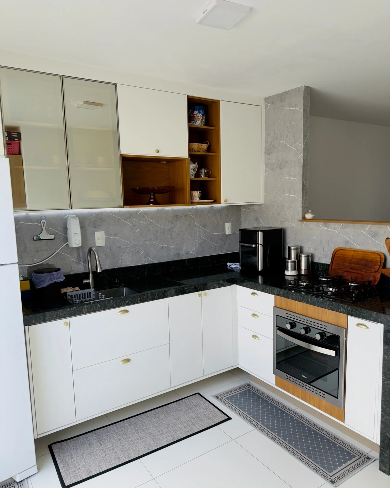 Cozinha branca em L com armários de vidro e cooktop embutido